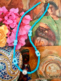 A turquoise blue beaded necklace with light blue evil eye beads and a white freshwater pearl accent.