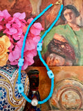 A turquoise beaded necklace with light blue square beads, dark blue eye-shaped beads, a white pearl, and a gold clasp.