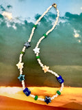 A beaded necklace with white round beads, blue and white star-shaped beads, blue evil eye beads, and small green spacer beads.