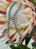 A dark gray pearl necklace, featuring a single larger white pearl bead at the bottom.