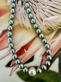 A strand of dark gray iridescent pearl beads with one larger white pearl at the end.