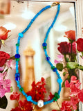 A beaded necklace with bright blue beads, smaller turquoise and green beads, and a white freshwater pearl.