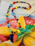 A colorful beaded necklace with star and heart charms. The necklace features a mix of red, blue, yellow, green, and orange beads, with a dark blue and red heart pendant inscribed with 'AMORE'.