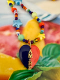A colorful beaded necklace with star and round beads, featuring a heart-shaped pendant split into navy blue and red halves with gold lettering that reads 'AMORE'.