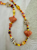 A handmade beaded necklace featuring orange seashells, starfish charms, and yellow, red, and purple beads.